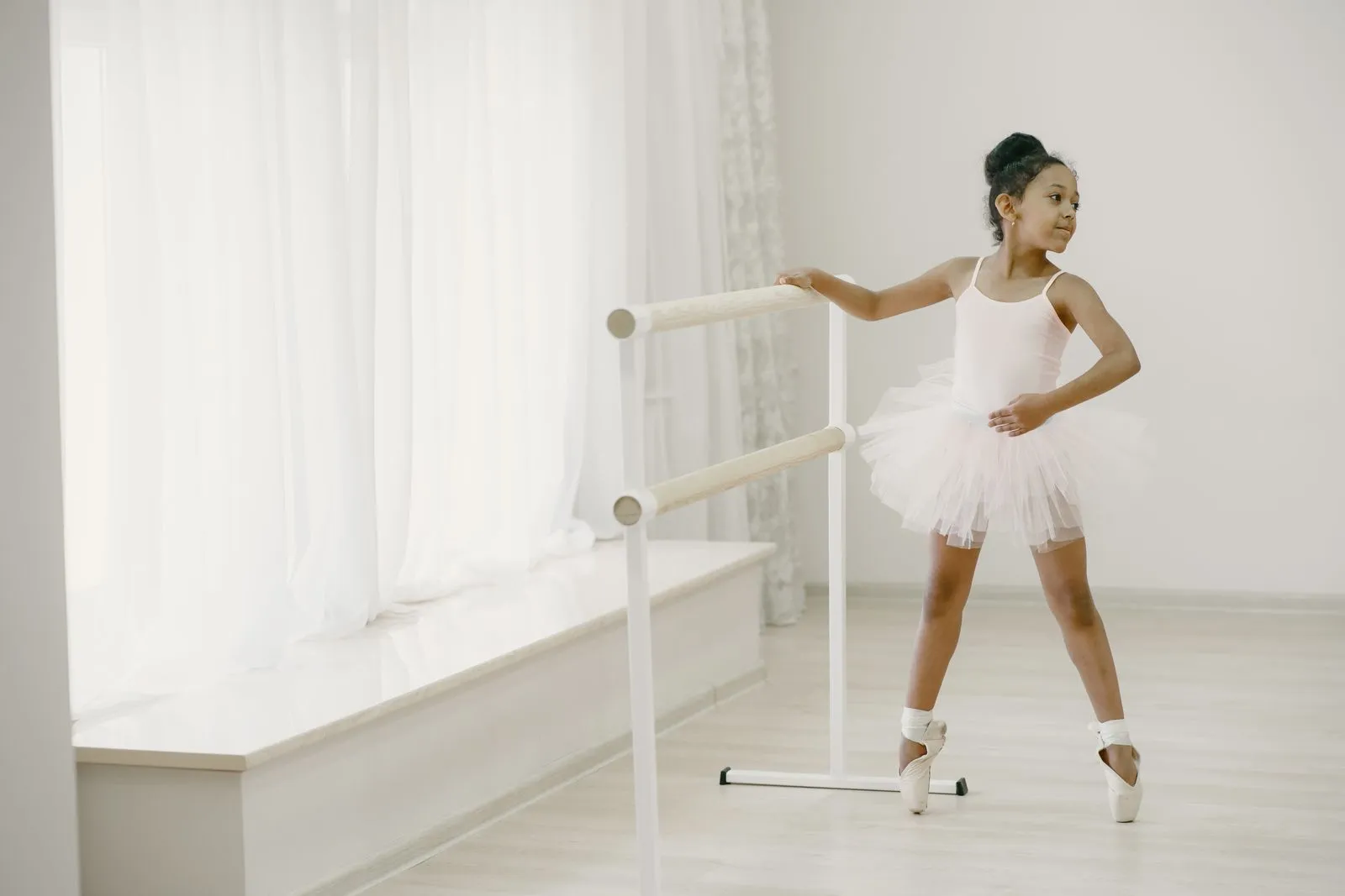 A young ballerina in a tutu practicing ballet at an indoor studio with natural light.